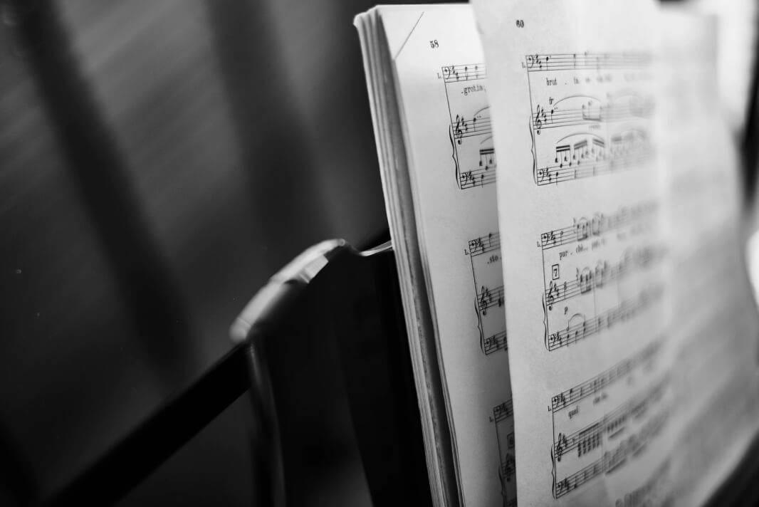Black and white close-up of an open book of sheet music on a music stand.