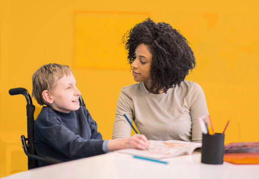 Cutout graphic highlighting young boy with disability in wheelchair smiling next to teacher against yellow background